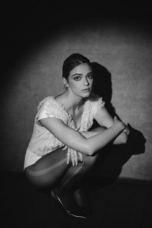 Dramatic black and white portrait of person in lace top crouching with strong shadow.