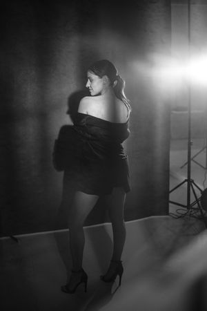 Dramatic black and white photo of woman in off-shoulder dress posing with studio lighting.