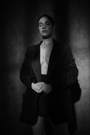Dramatic black and white portrait of figure in dark blazer against textured background.