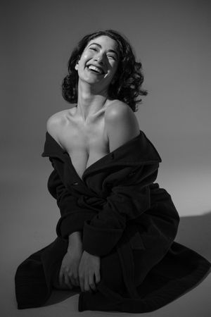 Black and white portrait of person laughing joyfully while wearing oversized jacket.