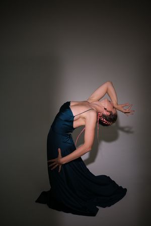 Dancer in navy dress performs expressive backbend in moody lighting.