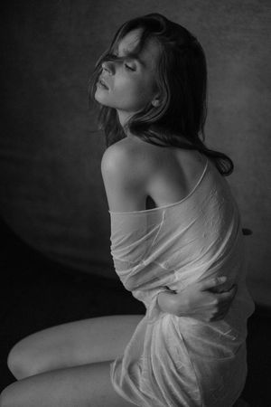 Artistic black and white portrait of woman in draped fabric with dramatic side lighting.