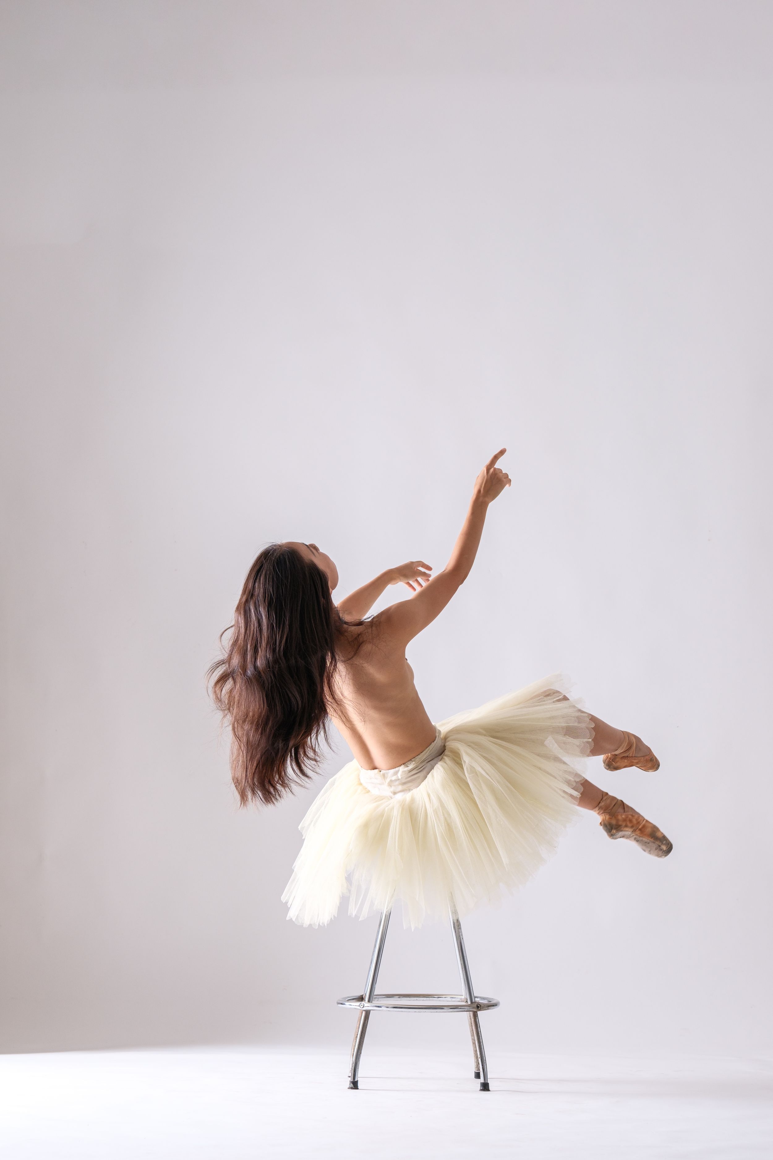 Artistic sequence showing a dancer in white dress performing movements on a chair against white background.