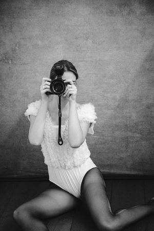 Artistic portrait of photographer in white lace bodysuit and tights holding camera.
