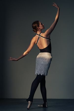 Ballet dancer in black leotard and white lace skirt poses gracefully.