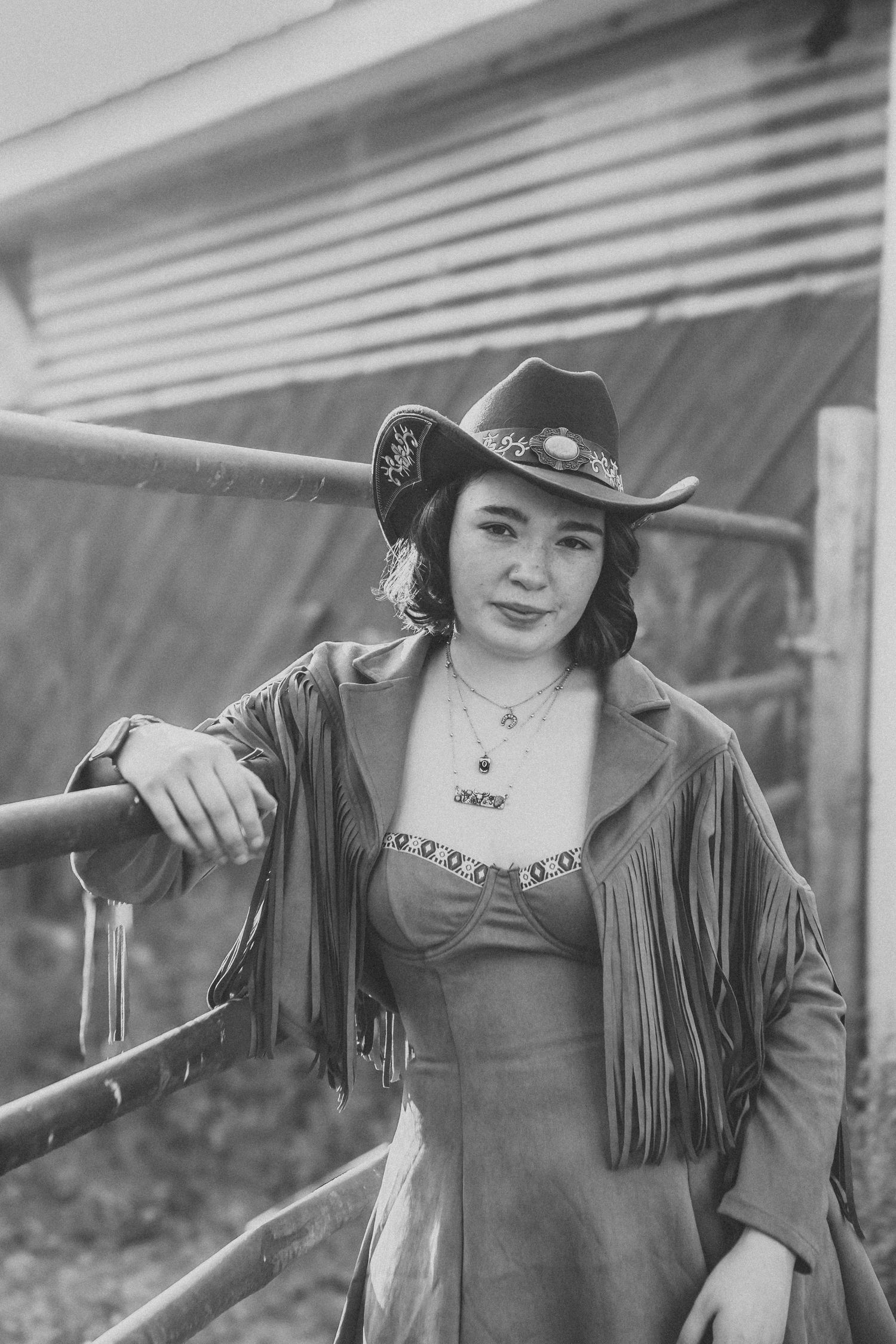 Person in western style clothing with fringe jacket and hat poses along a railing.