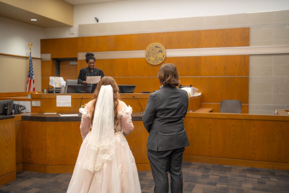 A couple signs documents during their courthouse wedding ceremony with an orange wall backdrop.