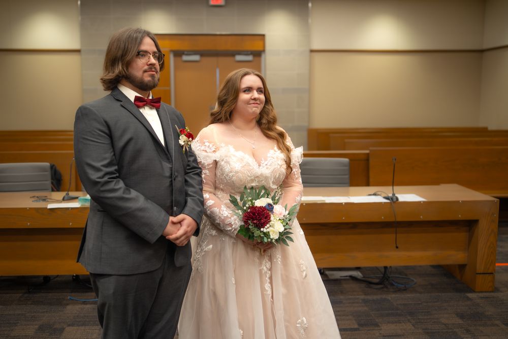 Wedding couple poses together in a courthouse hallway with wooden benches and interior lighting.