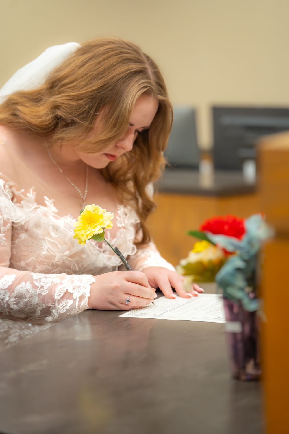 Person in delicate lace dress writing at a desk with yellow flowers and decorative elements.
