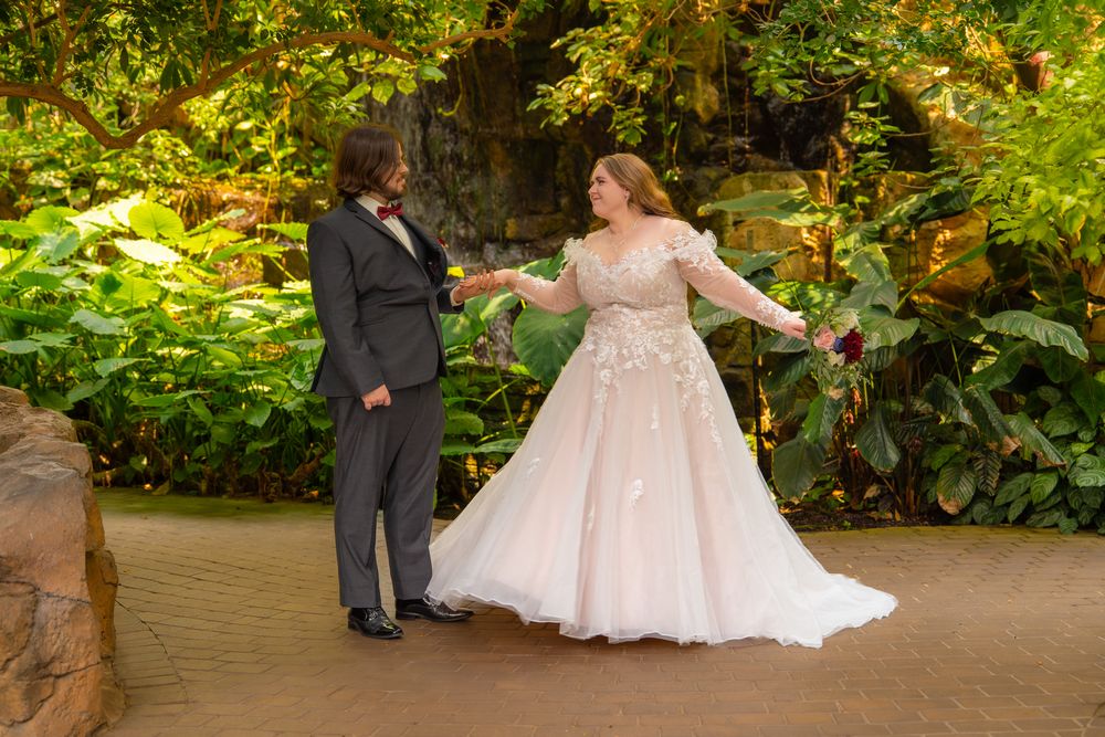 Newlyweds stand together in a lush garden setting surrounded by vibrant green foliage.