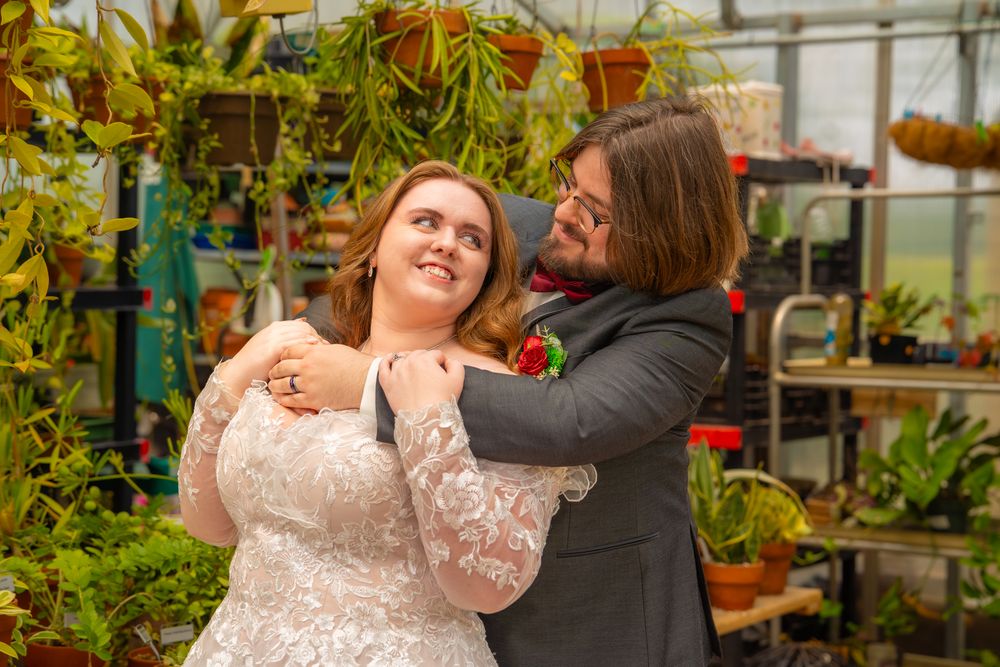 A wedding couple shares a romantic moment in a greenhouse filled with plants and flowers.