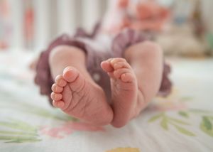 Tiny newborn baby feet resting on floral patterned fabric with soft pink blurred background.