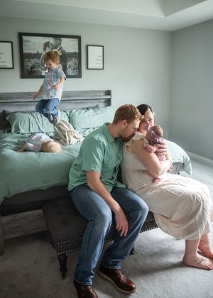 A cozy family moment on a bed with mint green bedding as a child plays in the background.