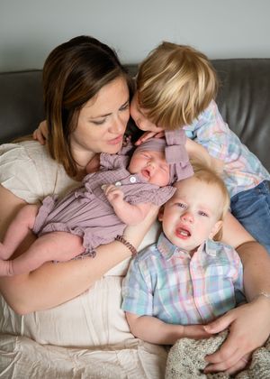 Family snuggles together on a gray couch, sharing an intimate moment with a newborn baby in purple.