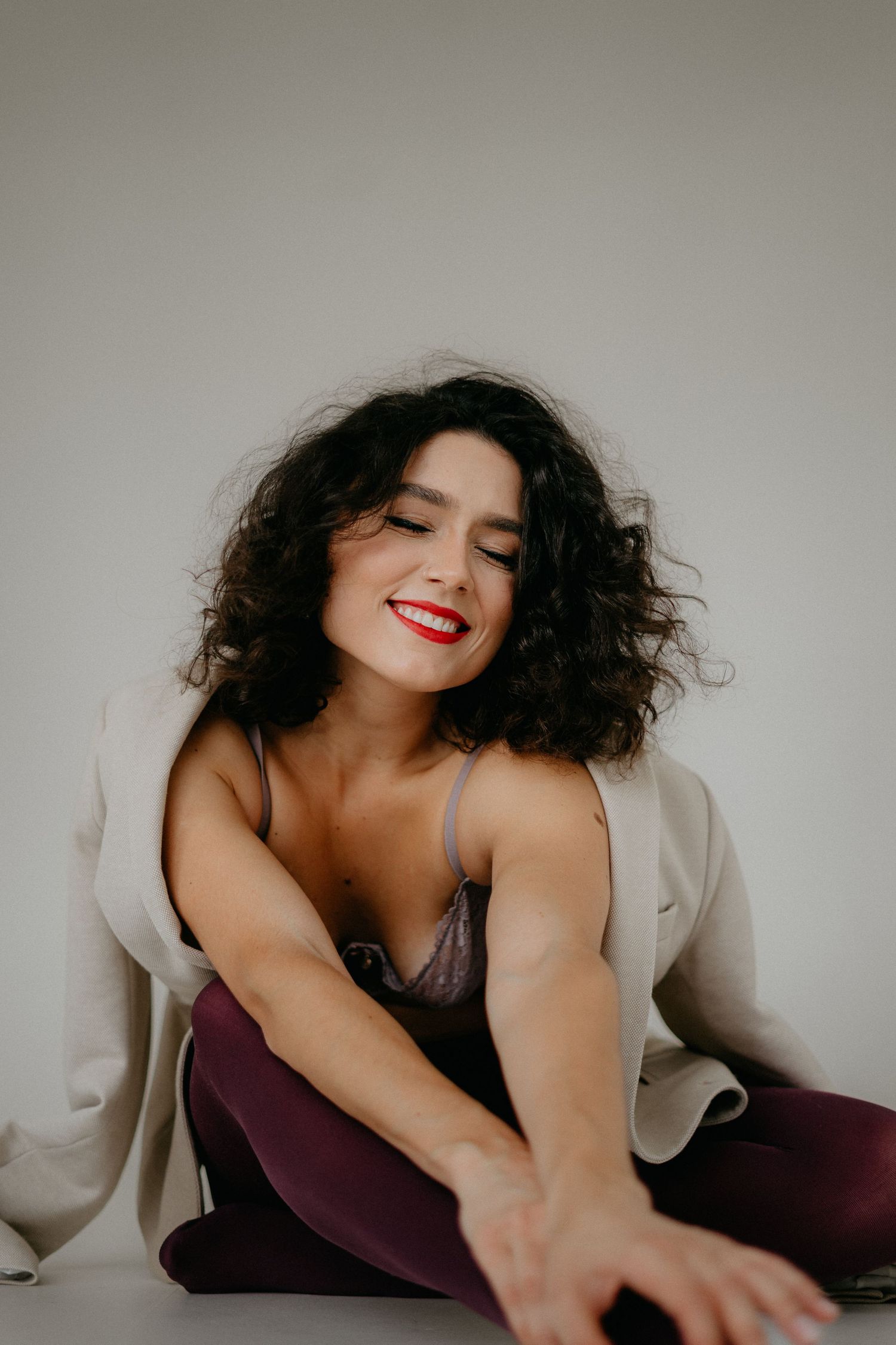 Intimate boudoir portraits with natural curls and expressive poses against light background.