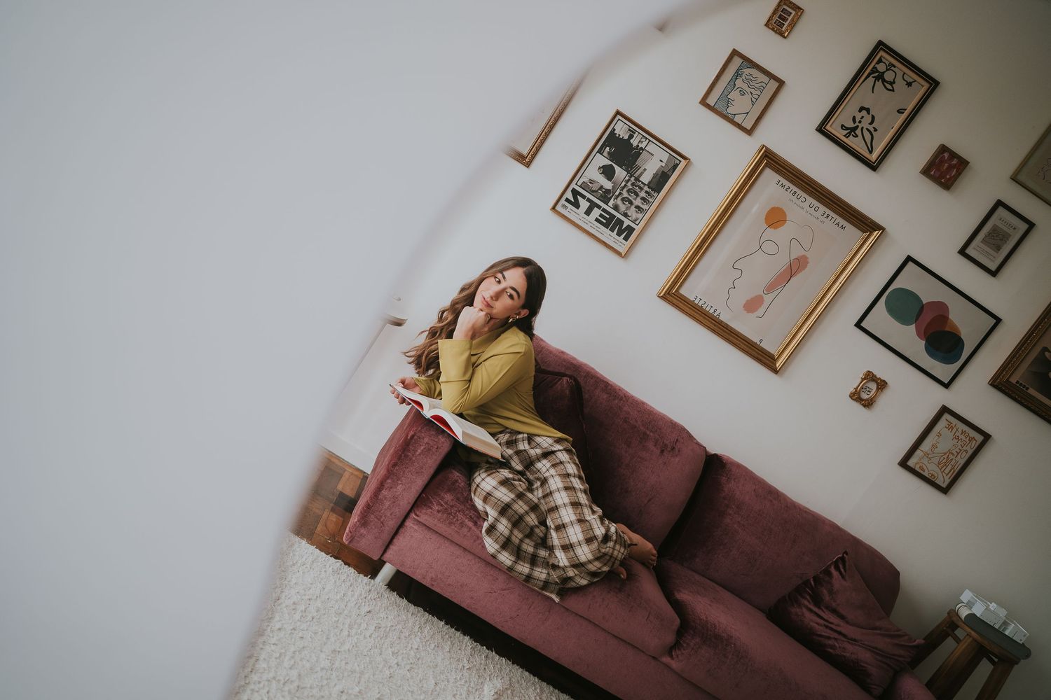 Cozy interior scene with someone lounging on pink sofa surrounded by framed artwork.
