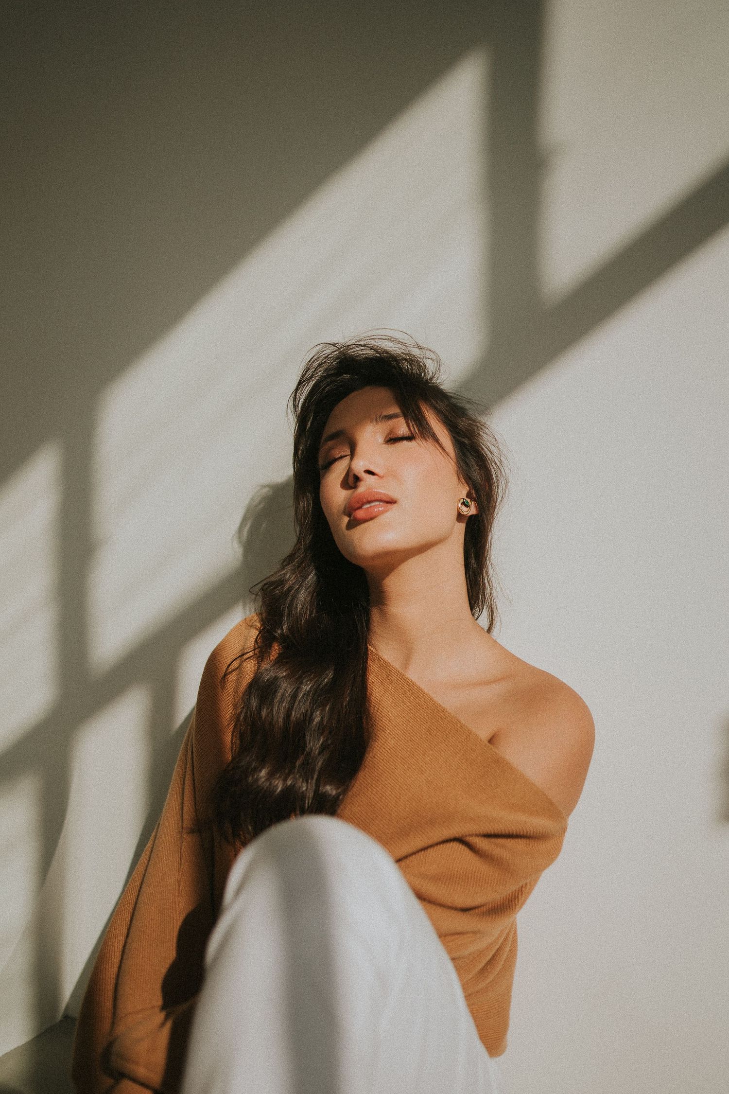 Artistic portrait series in warm light showing brown sweater against white wall with dramatic shadows.