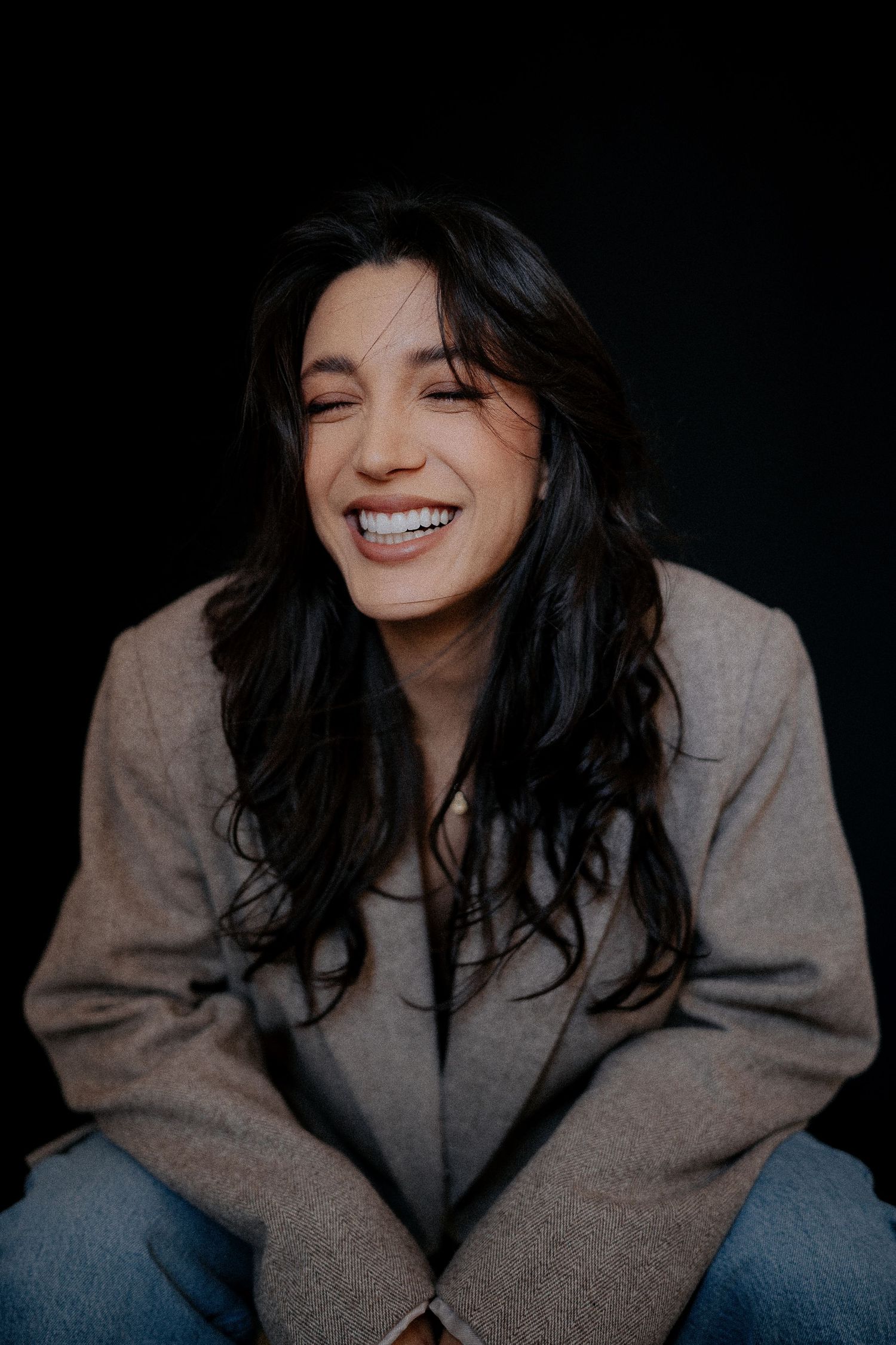 Candid portrait in grey blazer with natural smile against dark background.