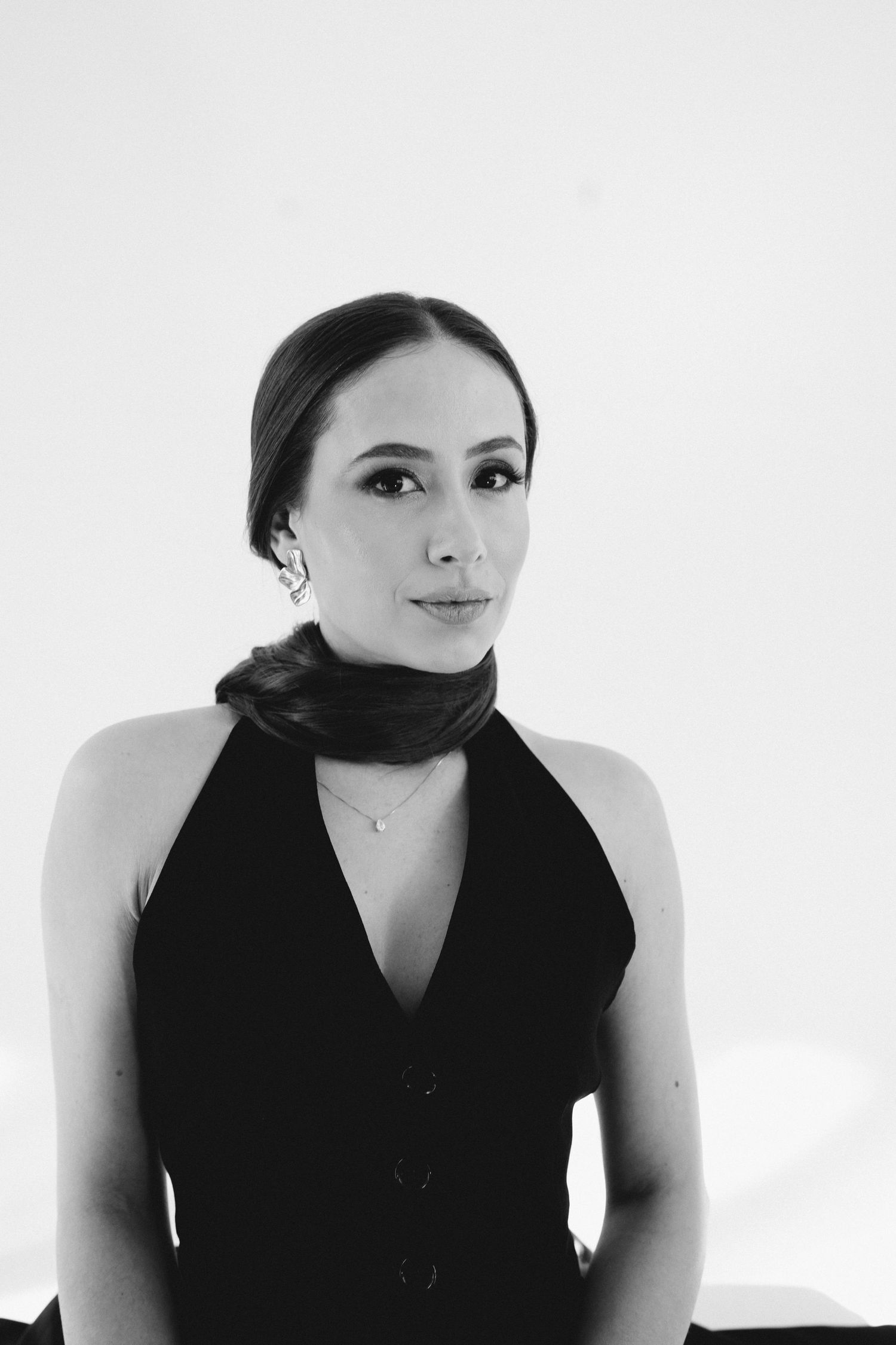 Black and white portrait of a woman wearing a black halter top and scarf with elegant makeup.