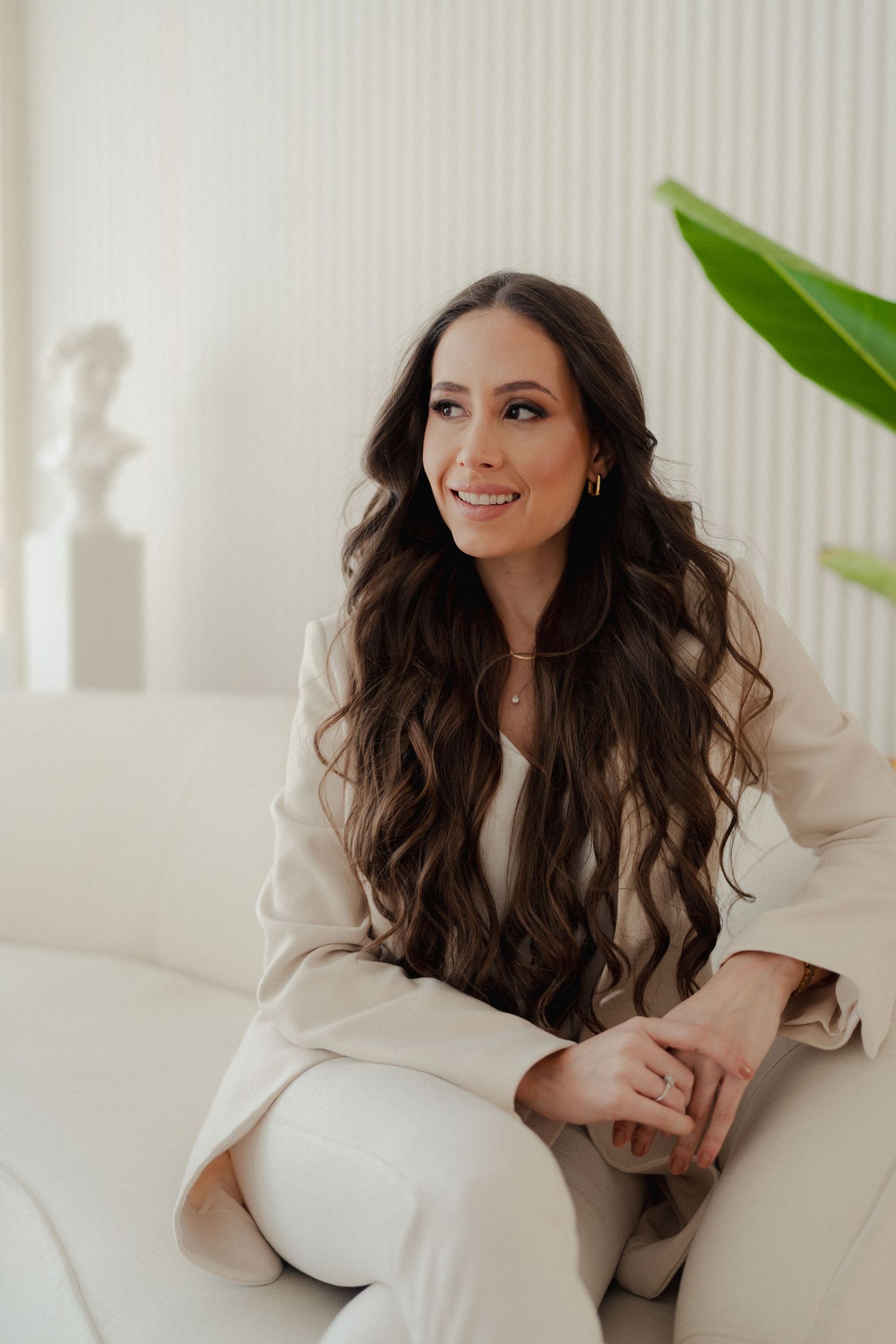 Elegant portrait on white couch with long wavy hair and cream colored outfit.