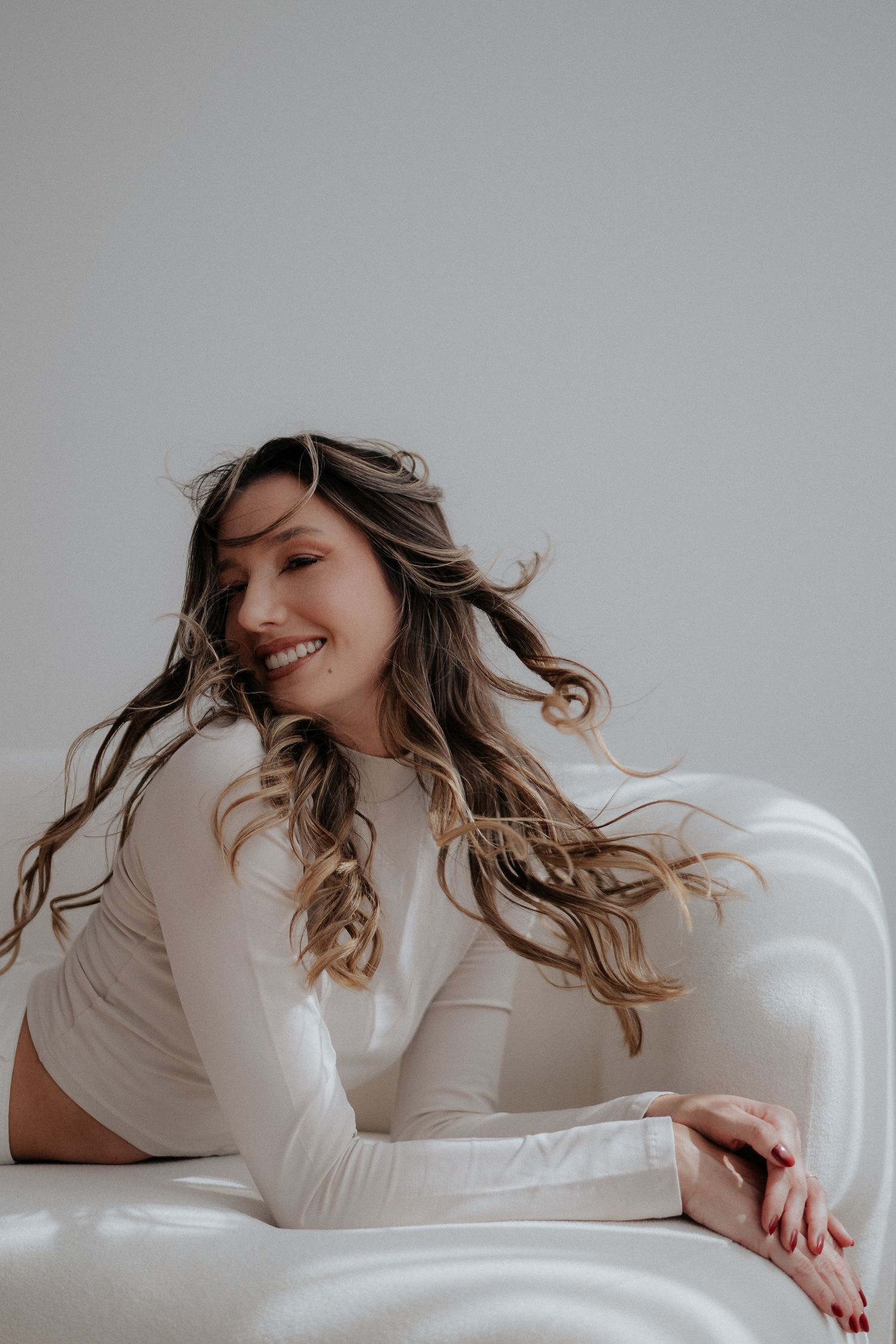 Lifestyle portrait of a woman in white lounging on couch with windswept hair.