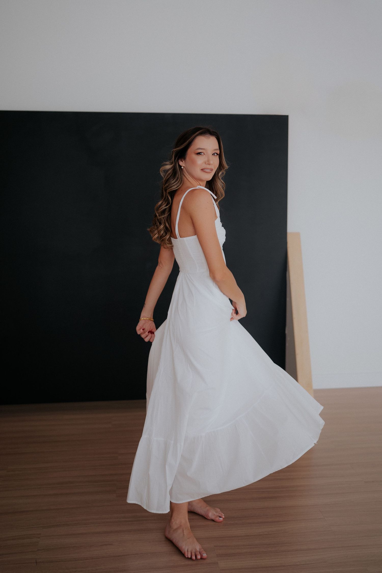 Woman in flowing white dress twirling gracefully against dark backdrop in studio setting.