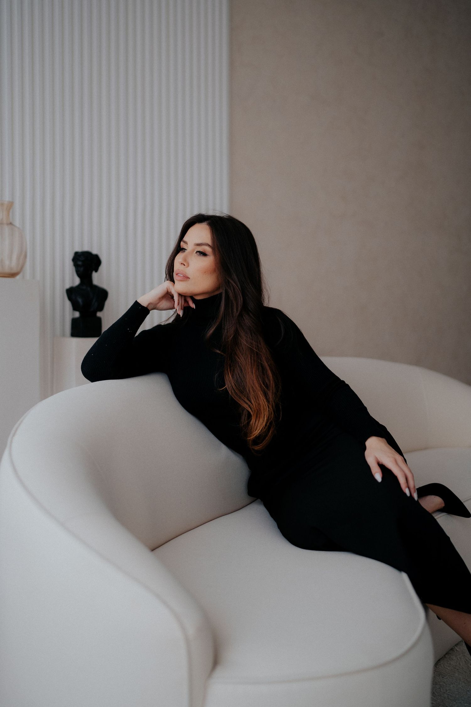 Elegant portrait of a woman in black dress reclining on white curved sofa.
