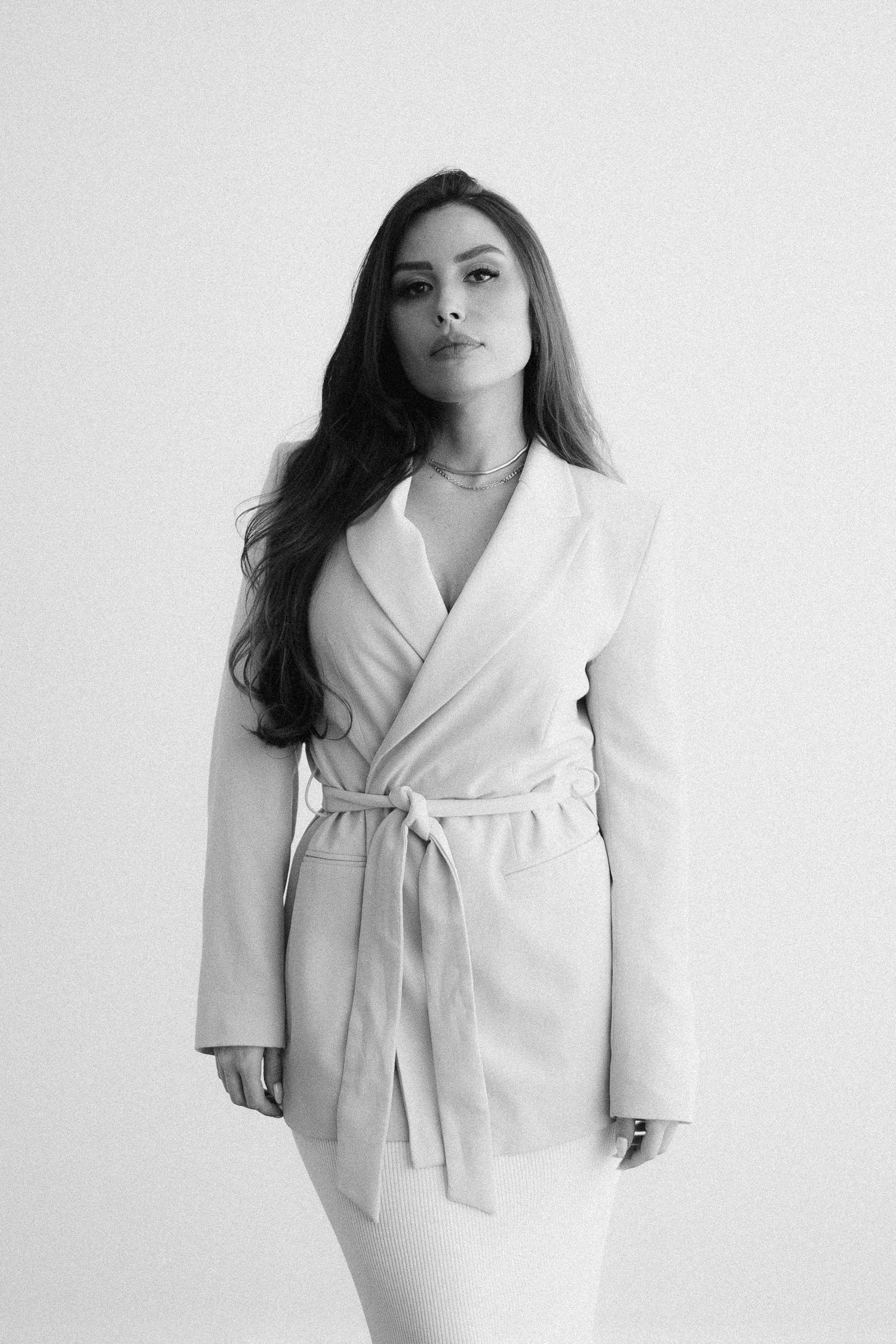 Black and white portrait of a model wearing elegant white wrap coat against light background.