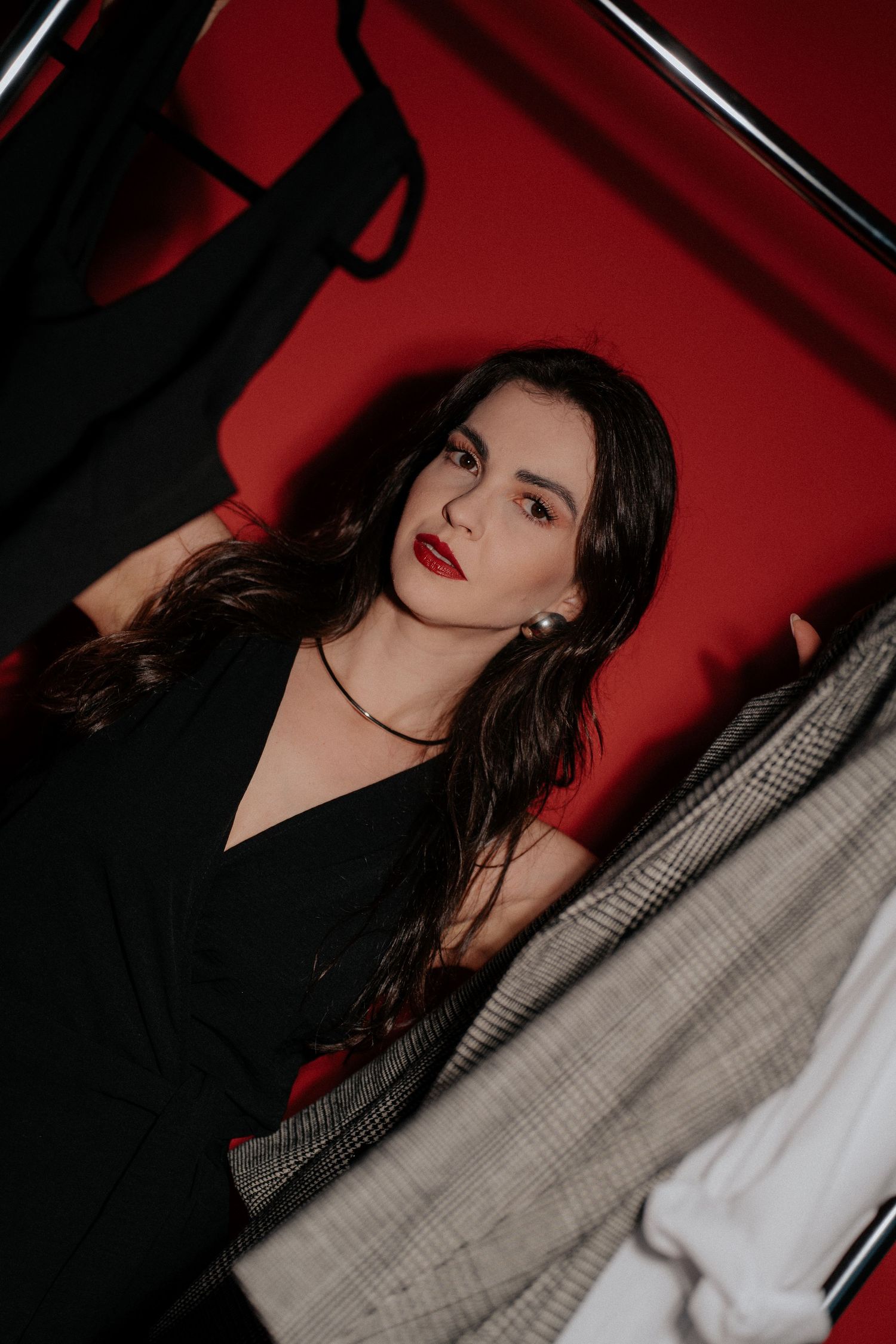 Dramatic portrait with red backdrop featuring model in black dress with bold lipstick.