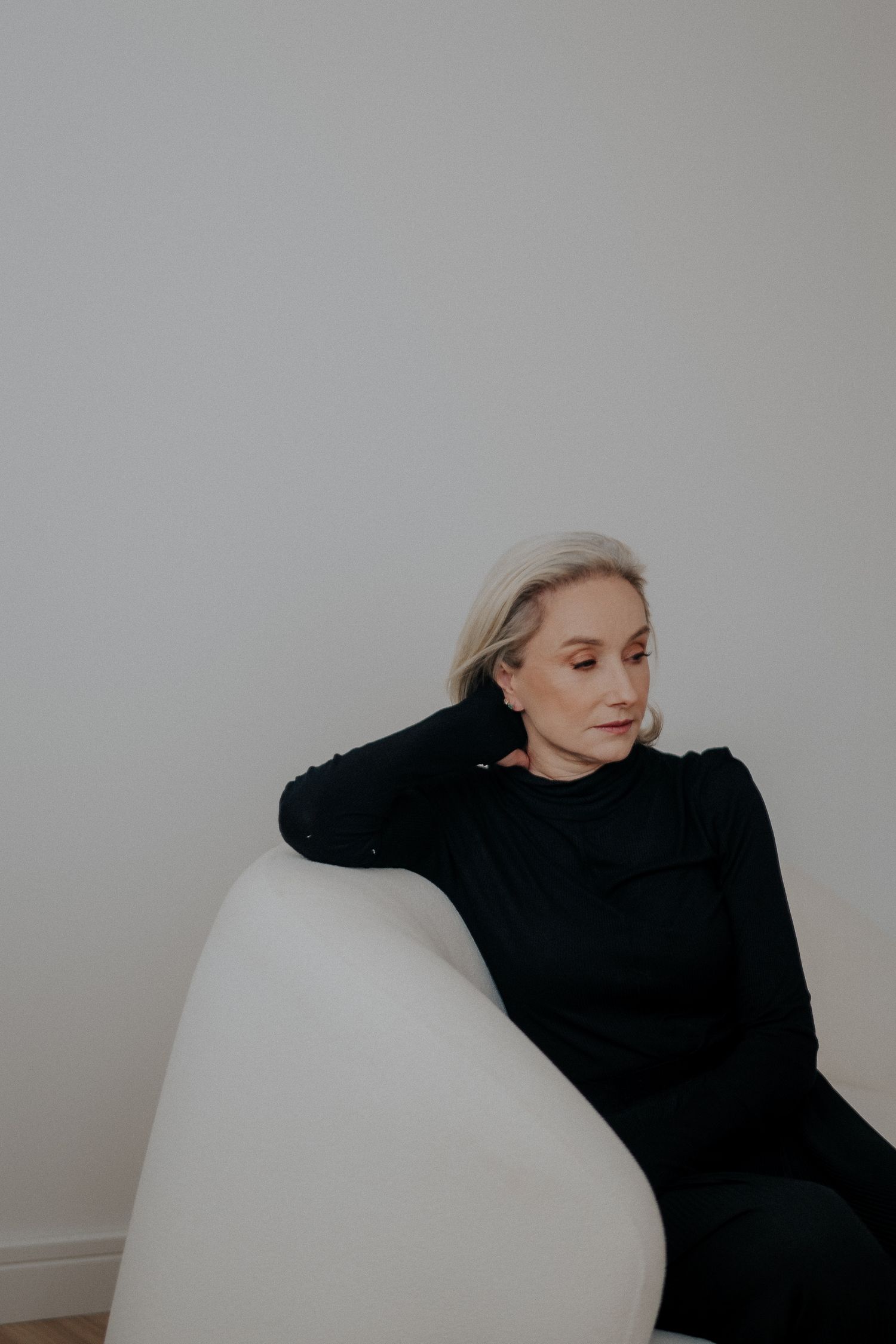 Artistic portrait of woman reclining in black sweater on white chair.