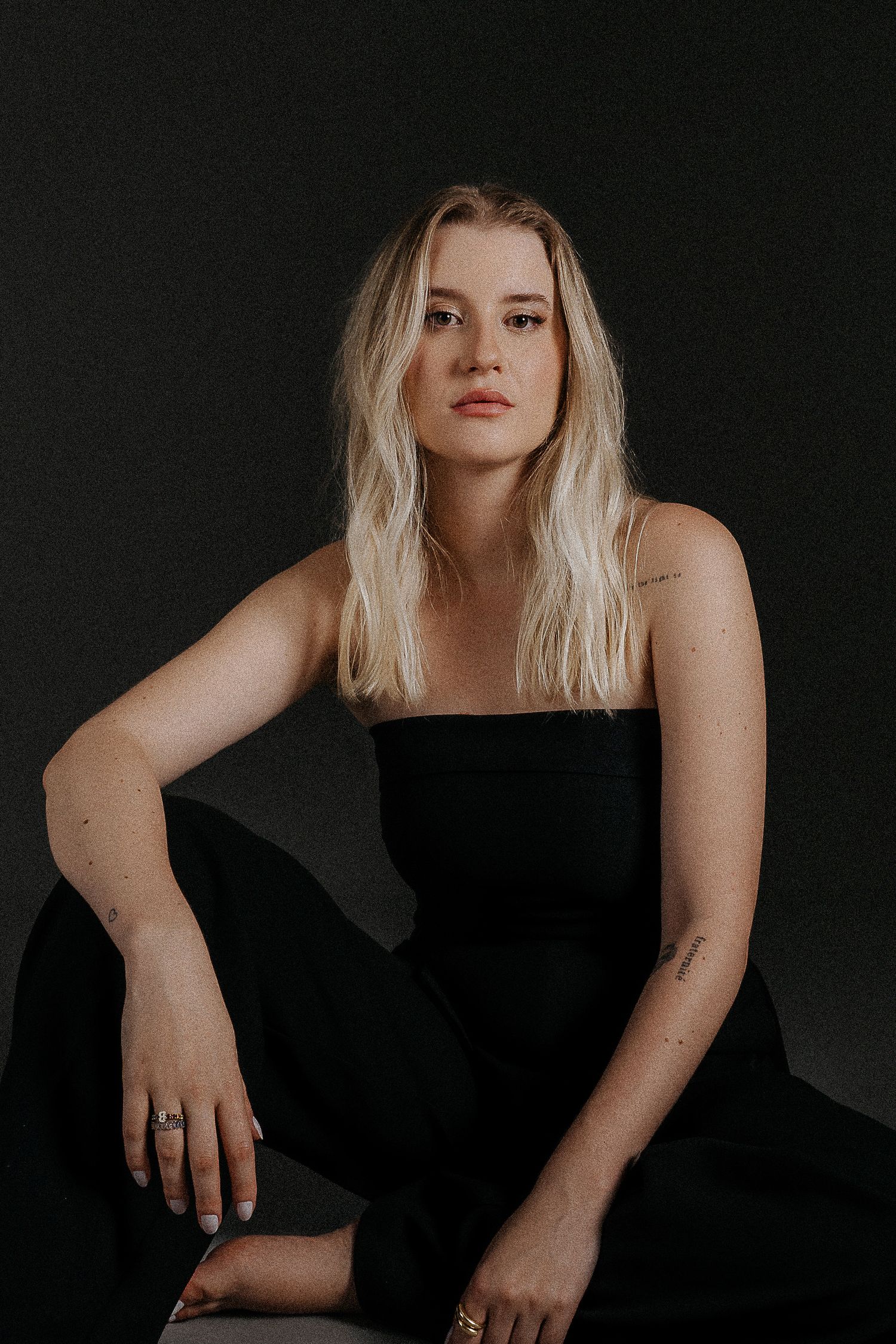 Moody portrait in black dress against dark background with natural styling.