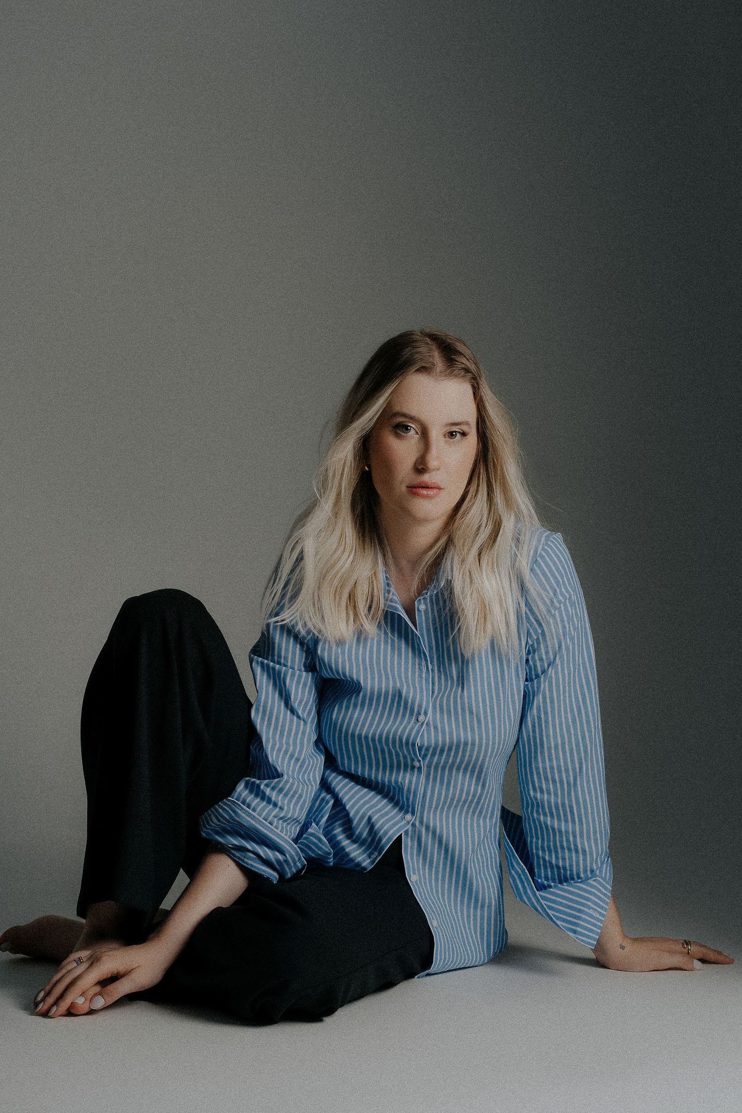 Casual portrait in striped blue shirt and black pants on light grey background.