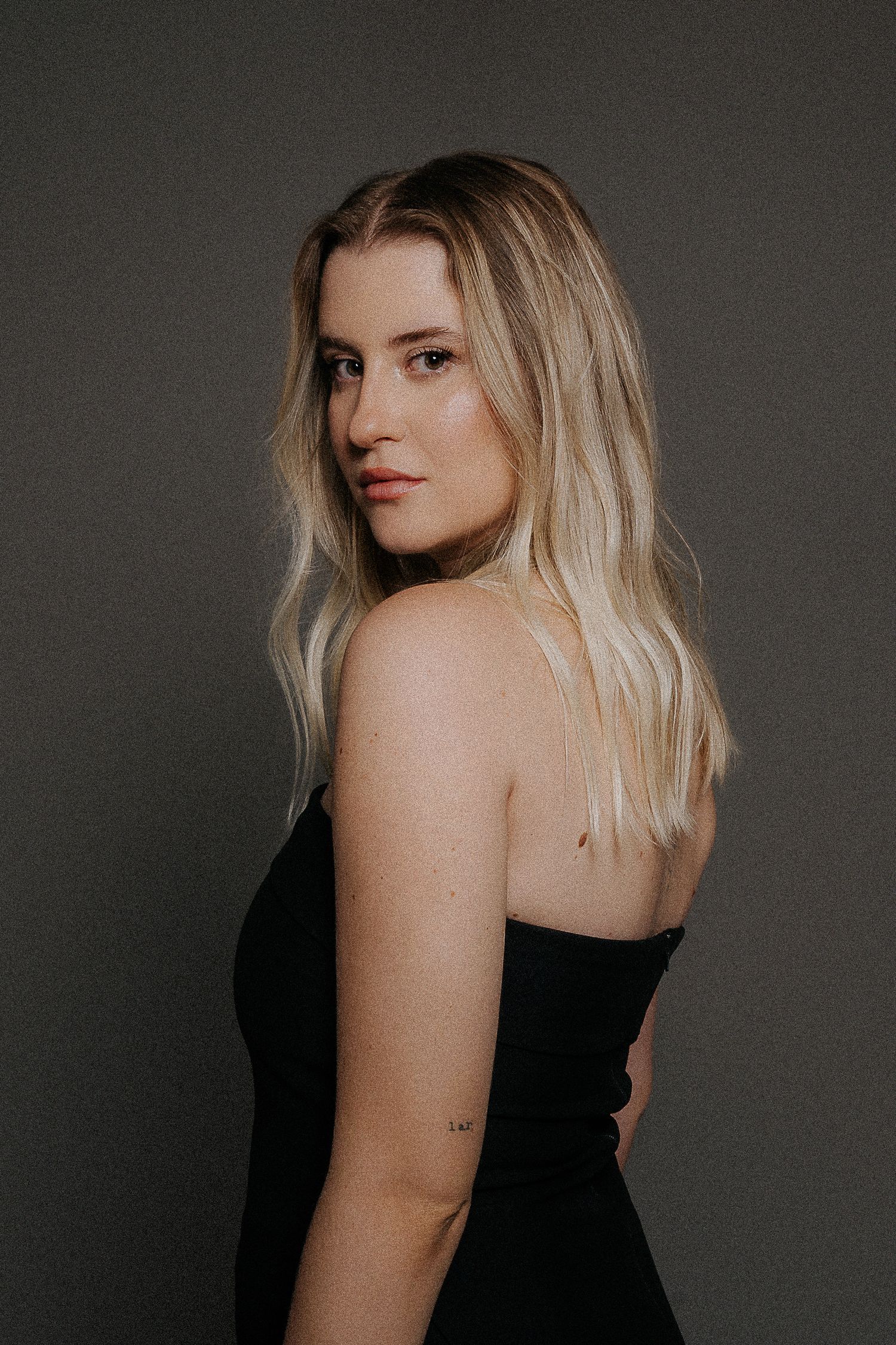 Artistic side profile portrait against dark background in black dress.