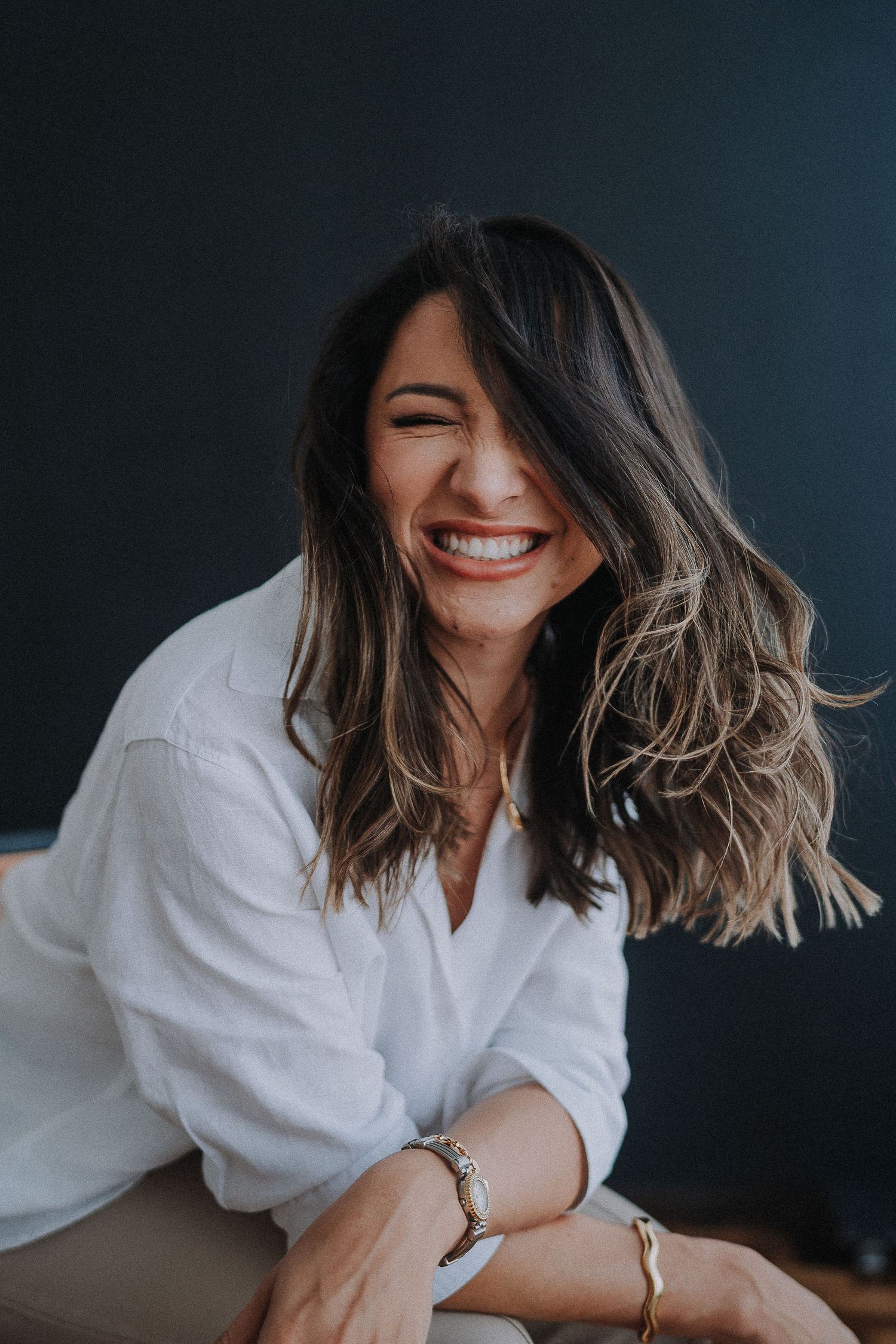 Joyful candid moment captured in white shirt against dark backdrop with hair in motion.