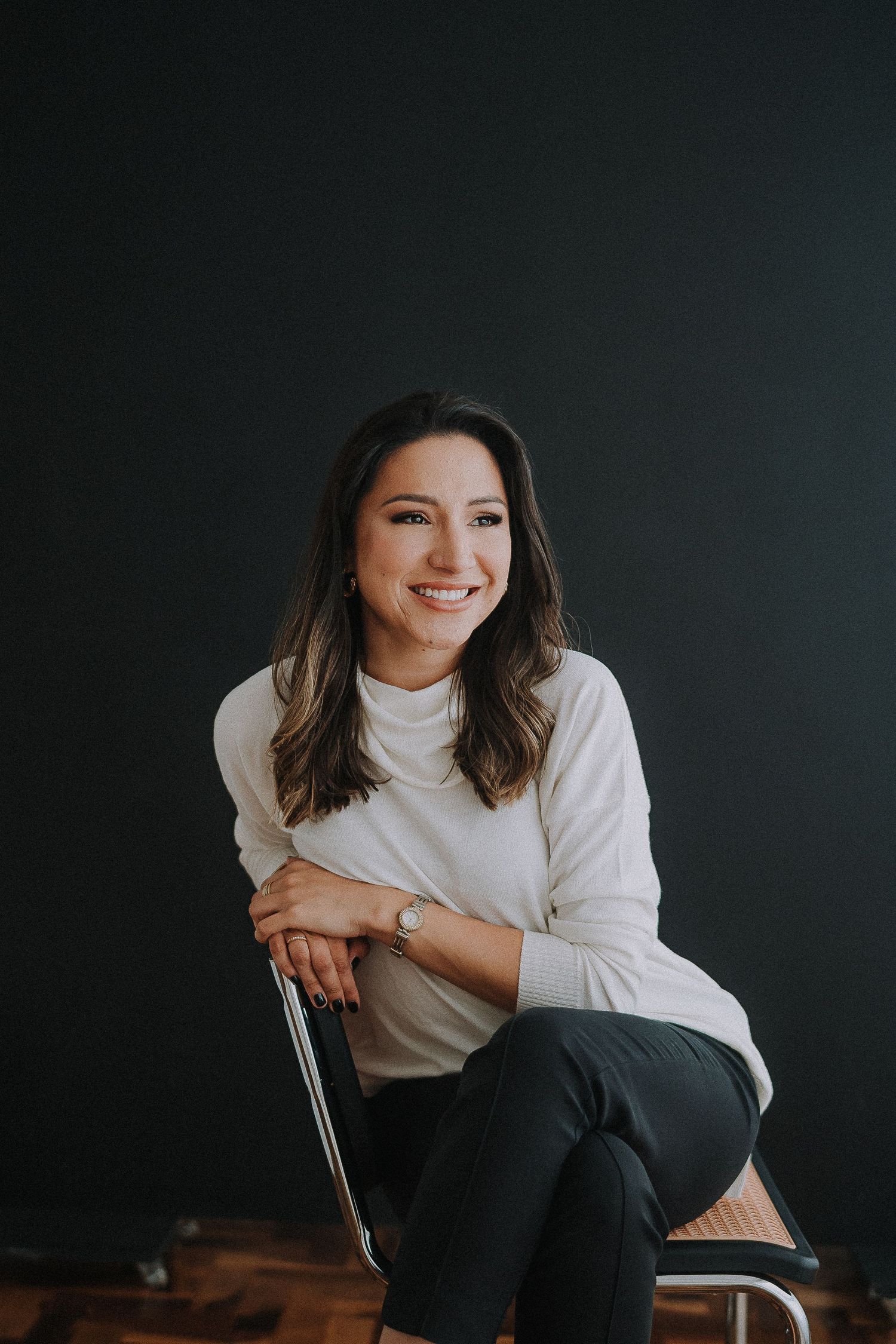 Professional headshot of someone in white blouse against dark background smiling warmly.