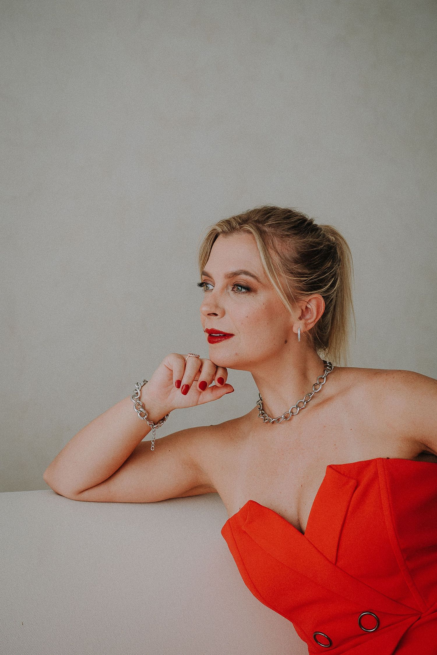 Fashion portrait of someone in a striking red dress against a minimalist gray background.