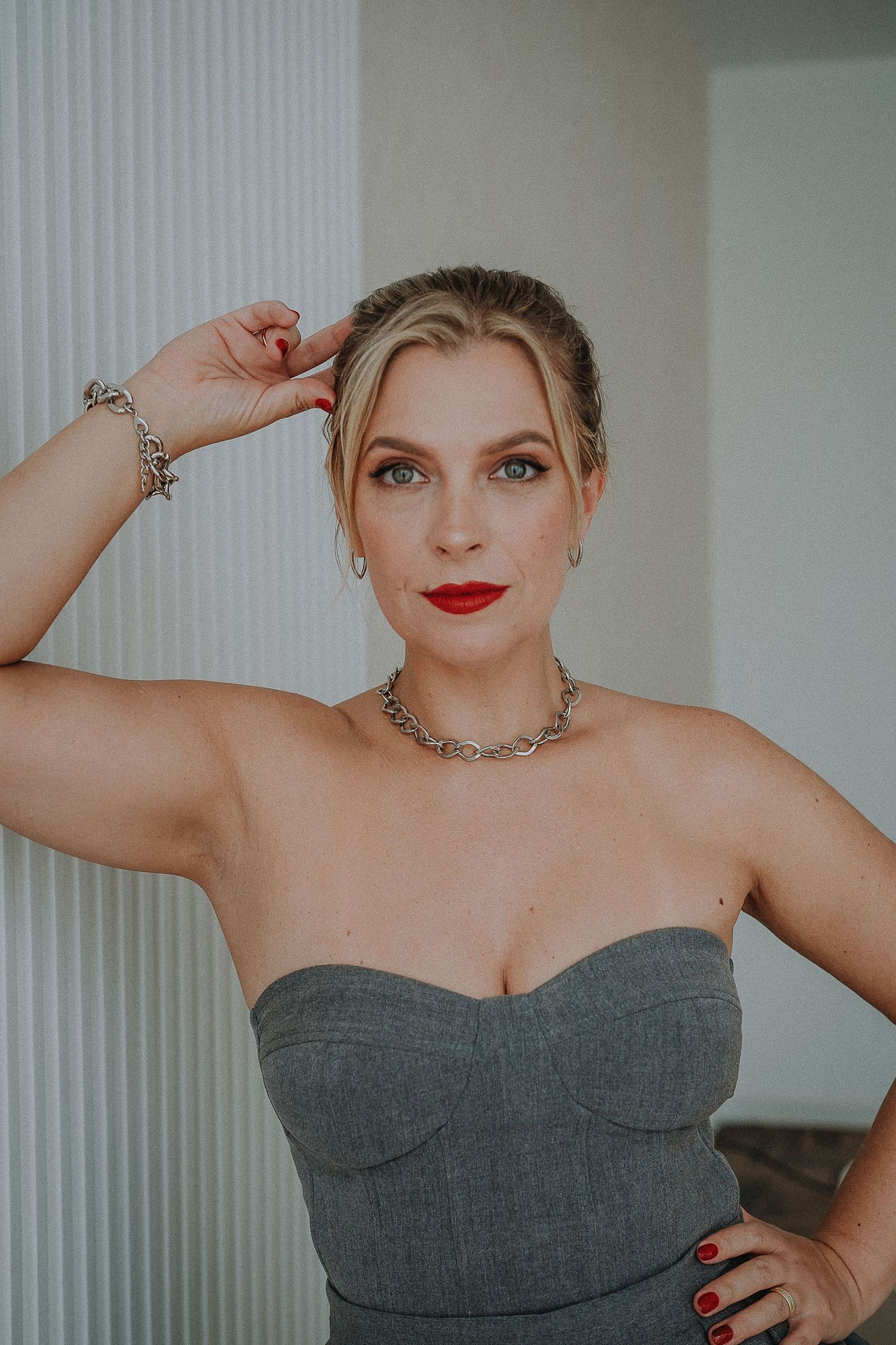 Elegant pose in a gray strapless dress with silver jewelry against white backdrop.