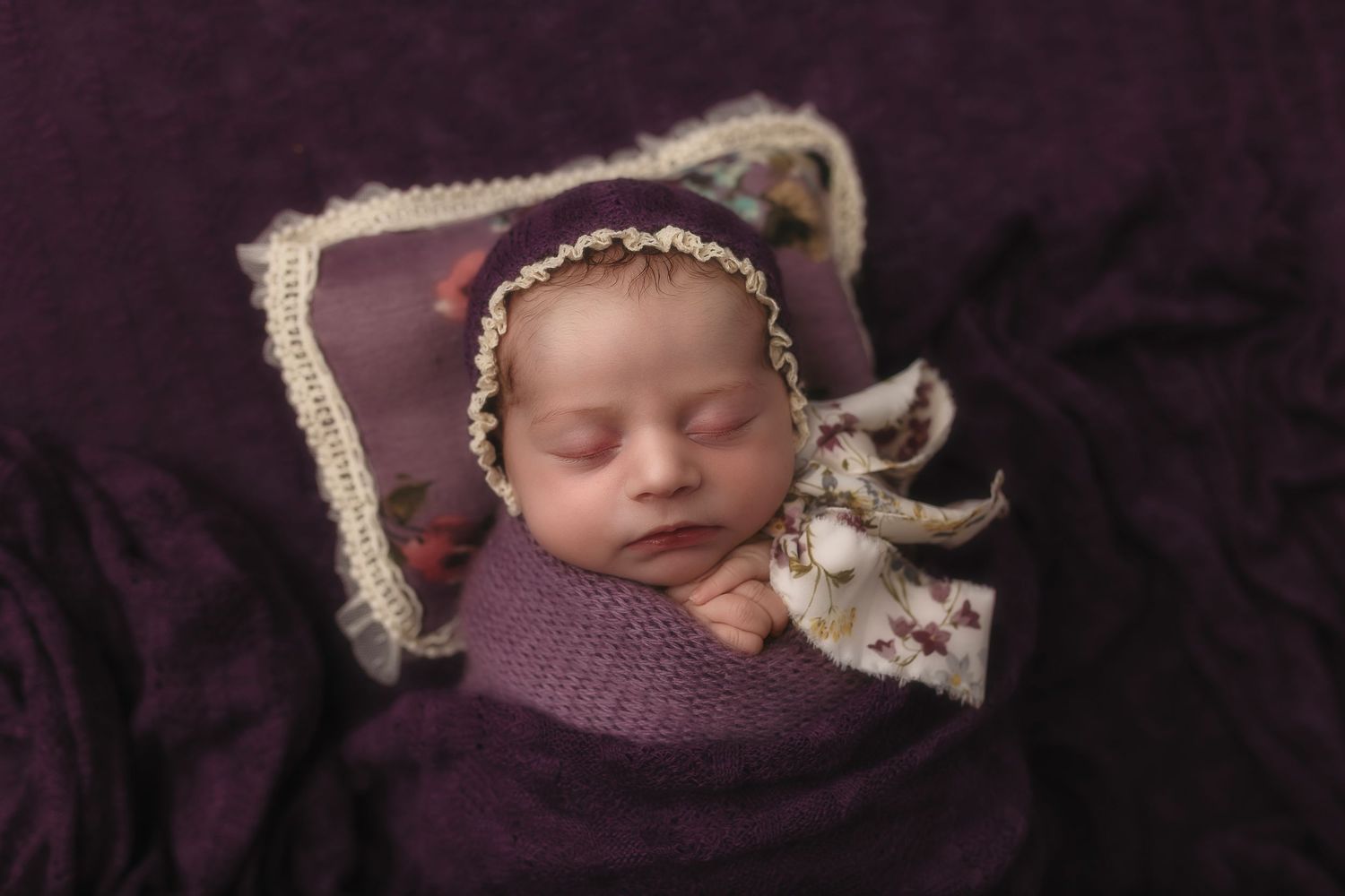Creamy dreamy newborn girl in purple floral bonnet and wrap captured by Somerset Portraits, a Charlottesville baby photographer.