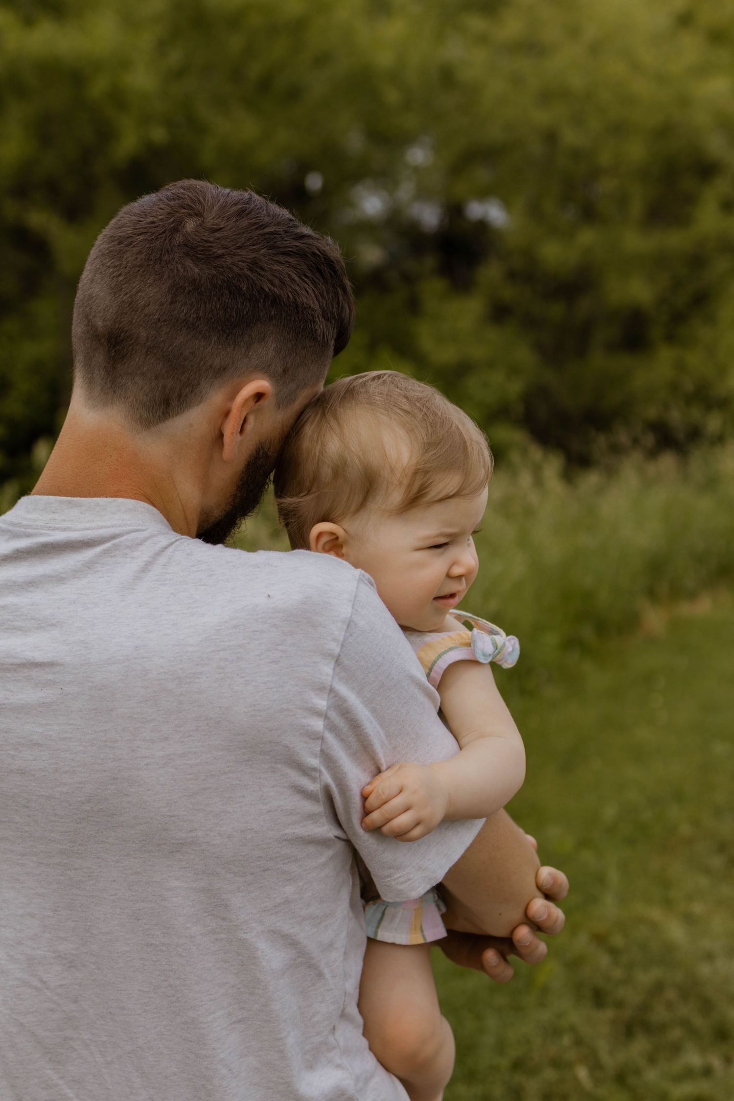 Parent holding and comforting a small baby in a series of tender outdoor moments against a green background.