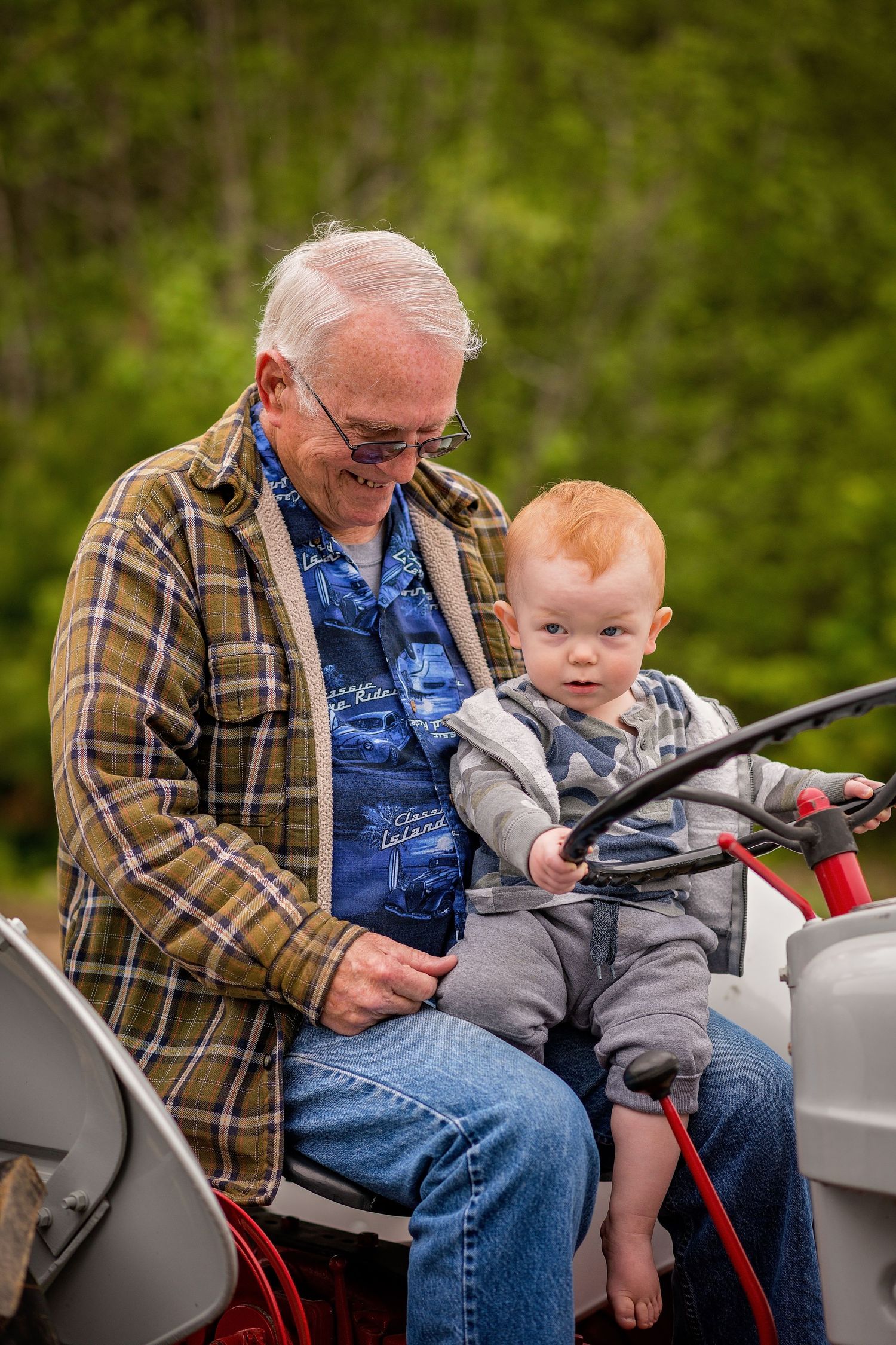 Two people sitting together on a gray tractor in an outdoor setting.