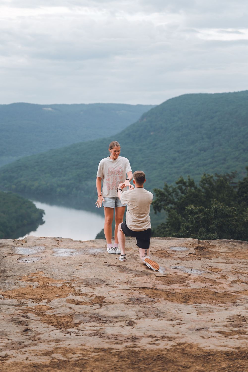 A sweet proposal moment unfolds on a mountain overlook with dramatic valley and river views in the background.