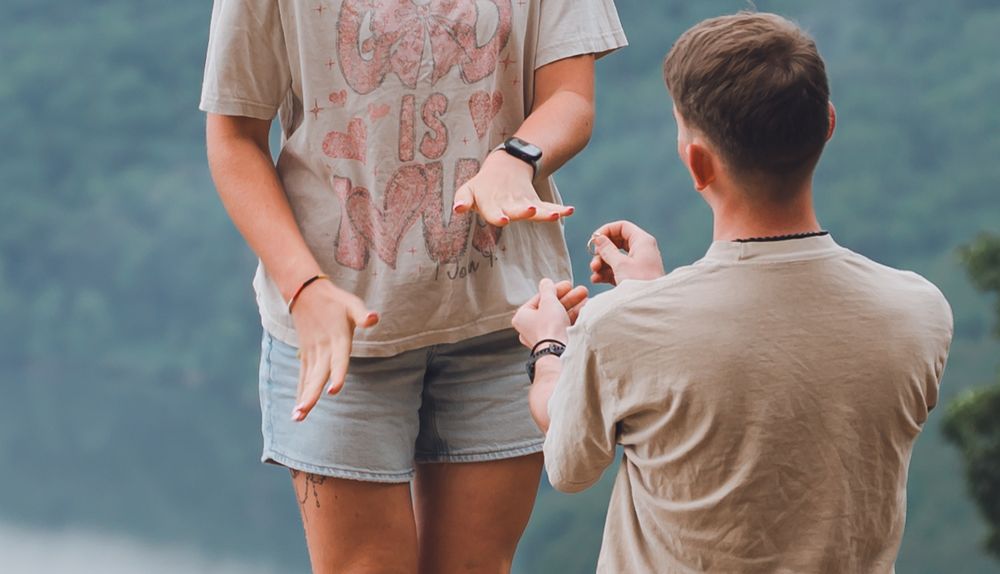 A proposal moment captured at a scenic lakeside location as someone kneels down on one knee.