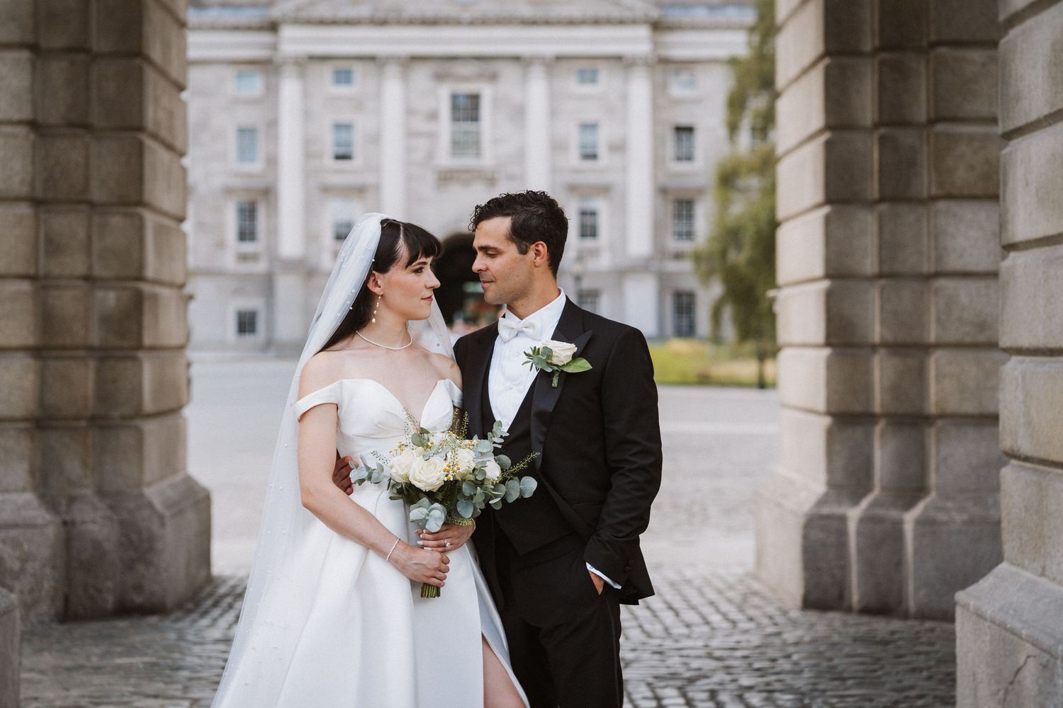 A bride and groom share an intimate moment under stone archways at their elegant outdoor wedding ceremony.