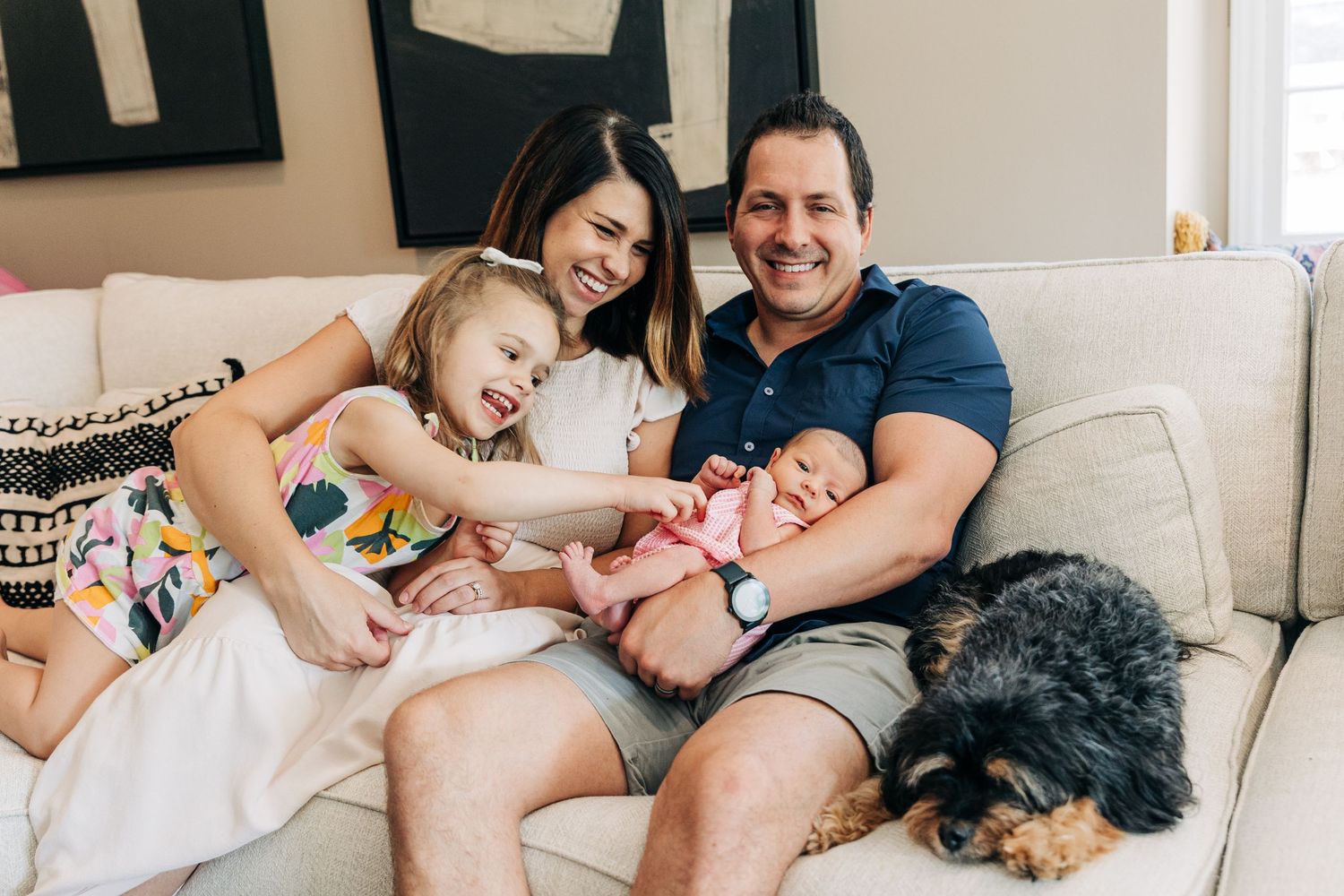Family relaxing together on white couch at home with their black dog.