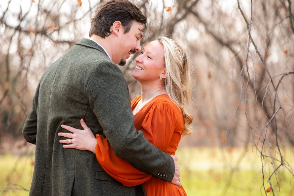A couple embraces in a romantic moment outdoors with autumn trees and natural scenery in the background.