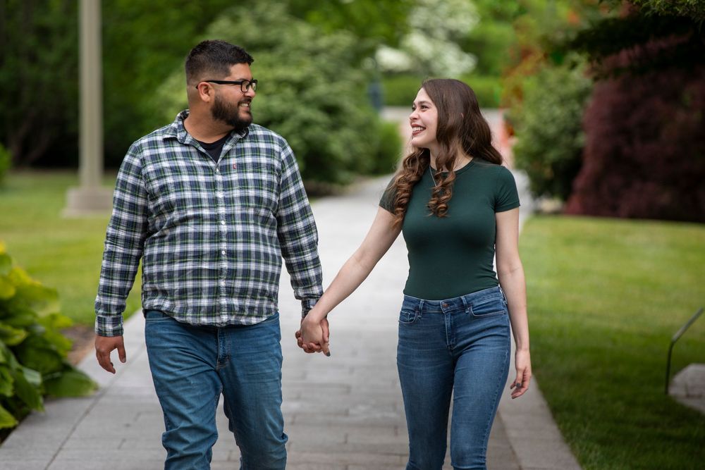 Couple in matching casual outfits holding hands while walking on grass path in a park setting.