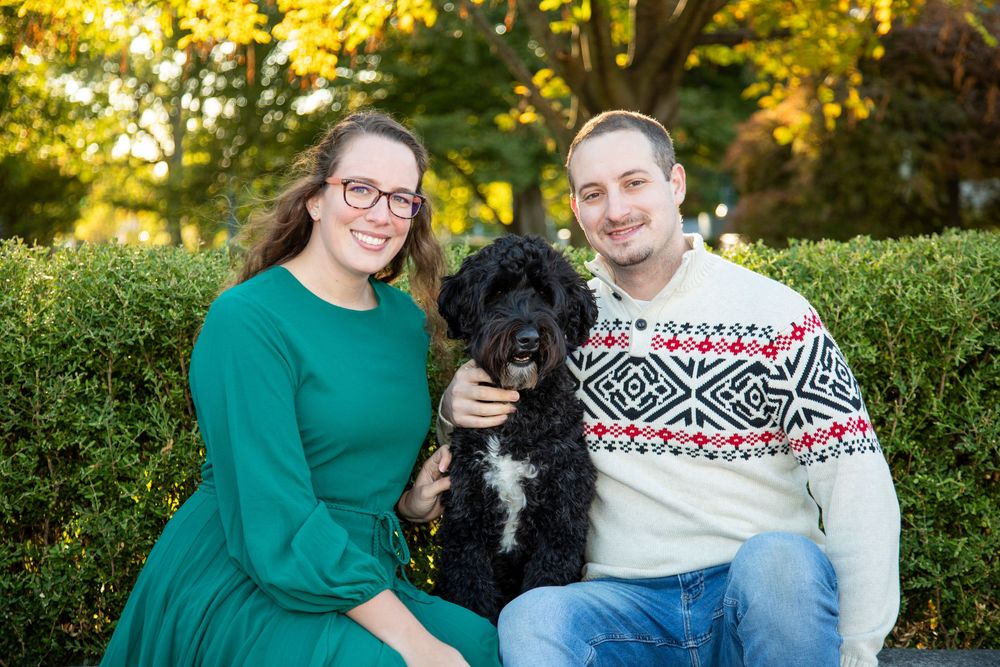 Couple with their black dog sitting together outdoors during golden hour autumn photoshoot.