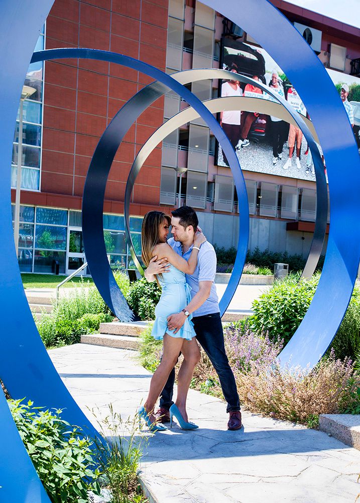 A couple shares an intimate moment under large blue sculptural arches in an outdoor garden setting.
