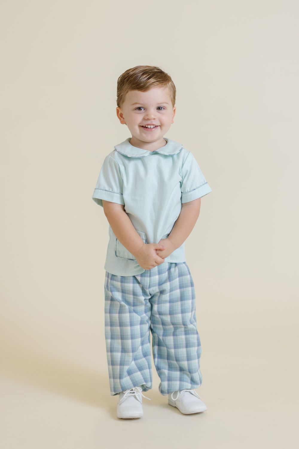 A toddler wearing a light blue shirt and plaid pants poses against a beige backdrop in four sequential photos.