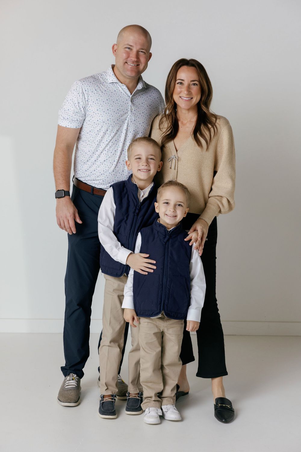 A family of four poses together against a light gray background wearing coordinated casual clothing.